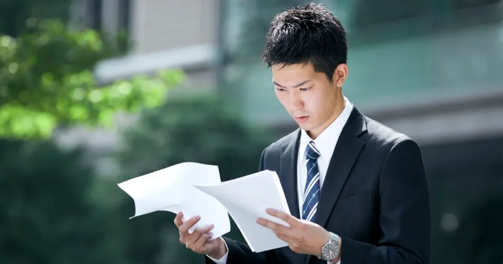 スーツ姿の若い男性が、真剣な表情で書類を確認している様子。転職活動中の不安や課題に直面している第二新卒を象徴するシーン。