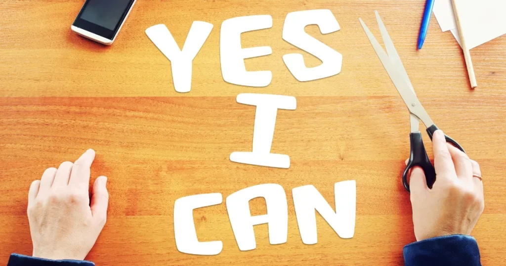 木目調のテーブルに「YES I CAN」と書かれた文字が並べられている。両手で文字を切り揃える様子が描かれ、前向きな姿勢や自己改善を表現している。