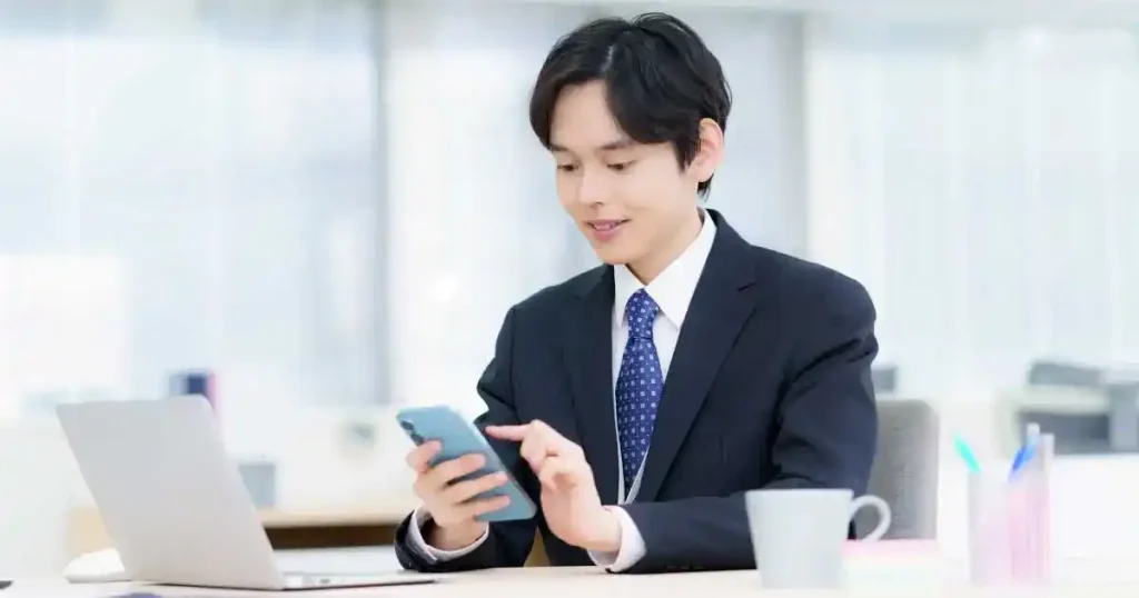 スーツ姿の男性がスマートフォンを操作中。転職活動で電話を使った問い合わせが適している状況を象徴するシーン。