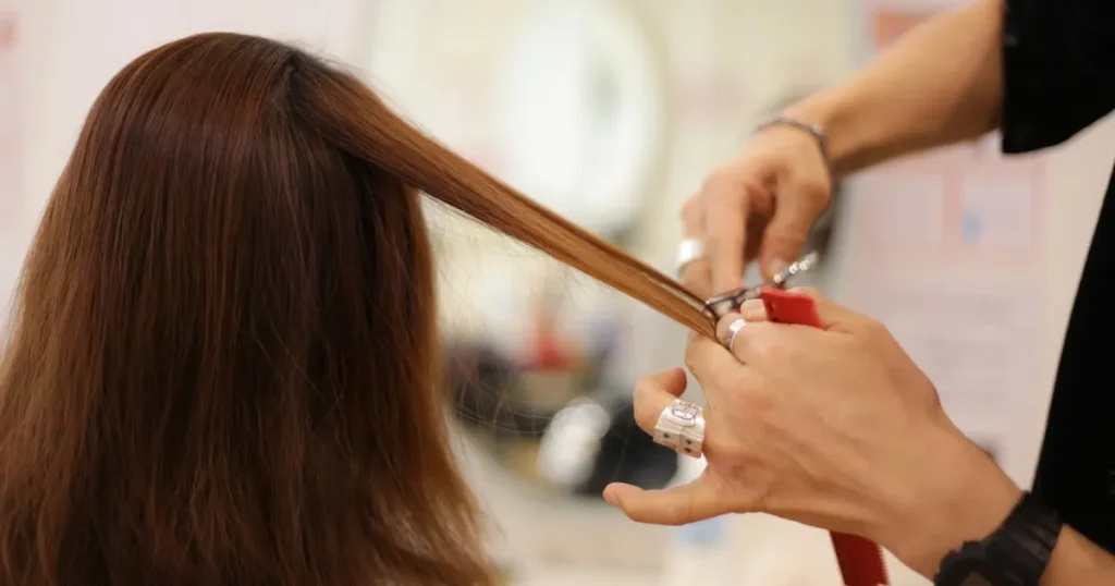 美容師がロングヘアの女性の髪を整えている様子。就活における面接で髪型が重要である理由について解説するセクションに関連するイメージ。