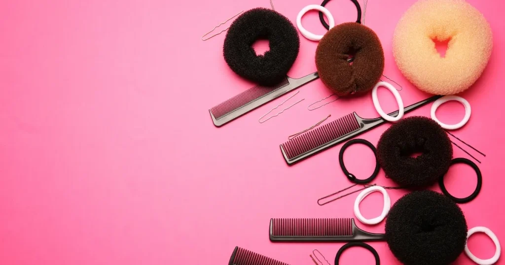 ピンクの背景に並べられたシニヨン用のヘアアクセサリーやコーム、ヘアピン。面接でロングヘアにシニヨンがおすすめな理由について解説するセクション用のビジュアル。